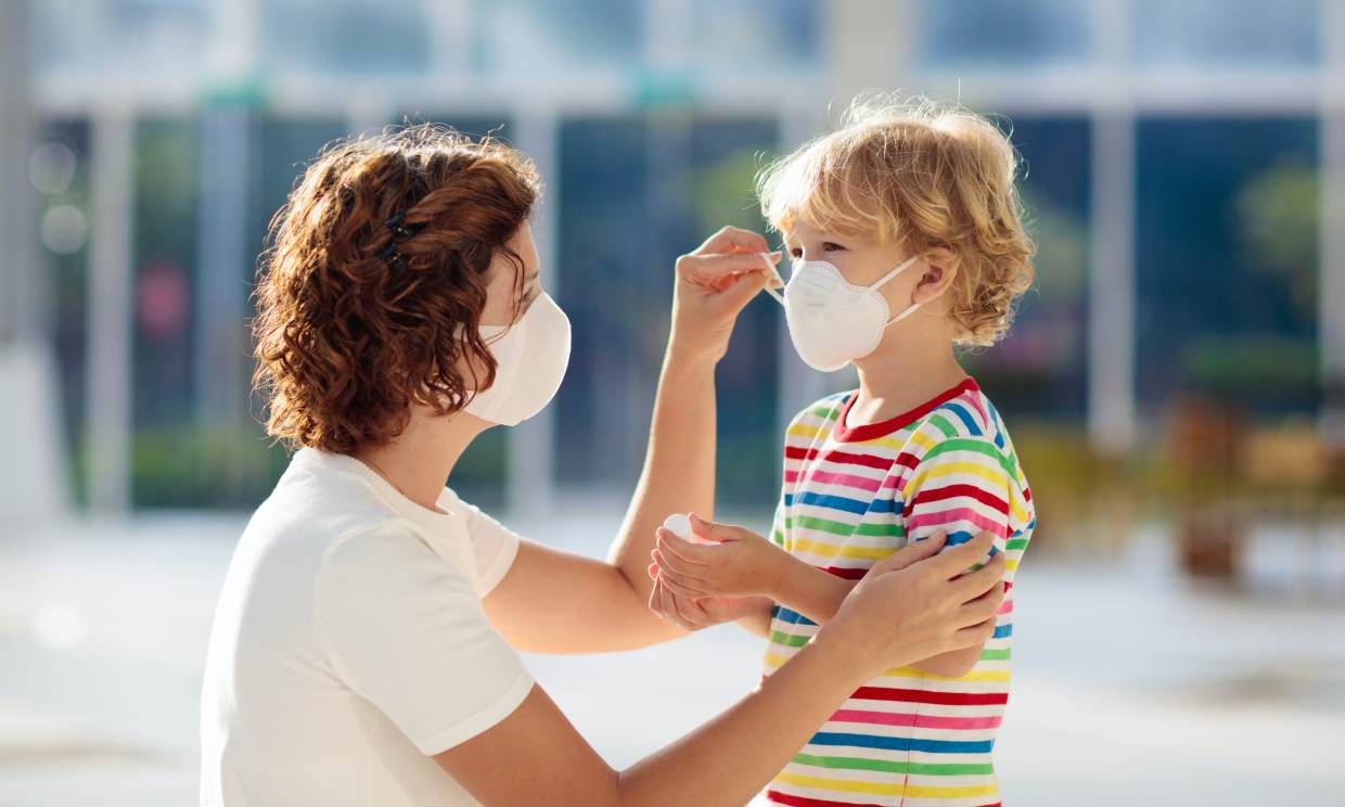 Una madre le coloca la mascarilla a su hijo / HOLA