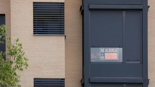 En la fachada de un edificio se ve un cartel de 'Se Alquila' bajo la persiana de uno de los pisos.