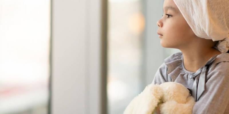 Niña con cáncer infantil mira por la ventana. GETTY