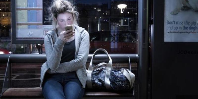 Chica mirando el móvil en una parada de autobús