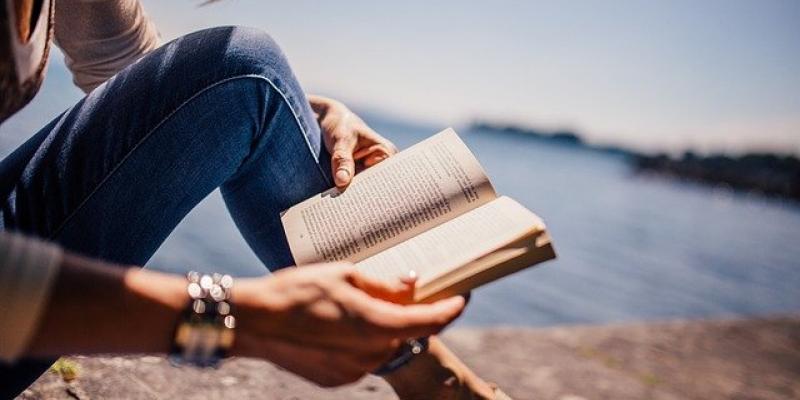 Niña leyendo un libro cerca de un estanque. Foto de Pixabay