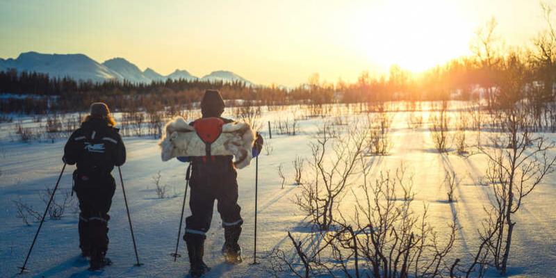 Dos personas caminan por la nieve mientras se pone el sol de fondo 