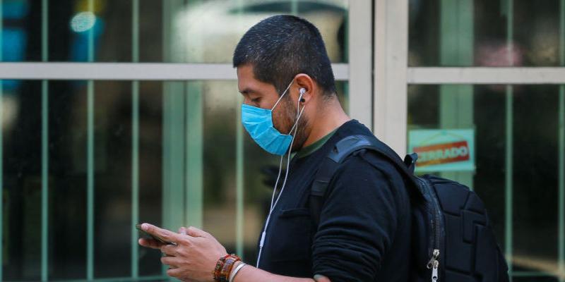 Un hombre con mascarilla mirando su teléfono Coronavirus | Un hombre con mascarilla consulta su teléfono / Getty