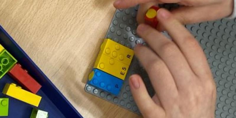 Manos de un menor jugando con las piezas de LEGO en Braille 