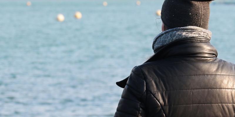 Una mujer, abrigada, mirando a un lago en un día soleado