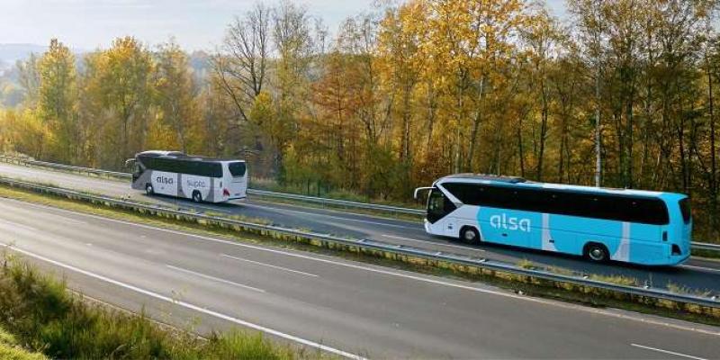 Dos autobuses de la compañía Alsa circulan frente a un bosque