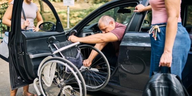A caregiver assists a person with a disability as they transition from a car to a wheelchair. / Envato Persona con discapacidad saliendo de su coche