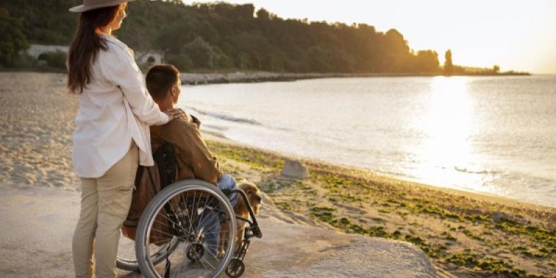 Hombre en silla de ruedas en la playa acompañado de una mujer