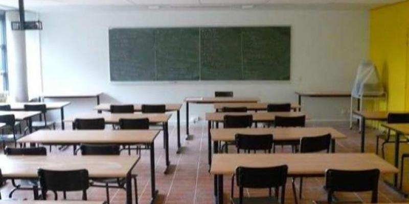 Aula vacía un pasillo central y los pupitres a derecha e izquierda, pizarra verde al fondo 