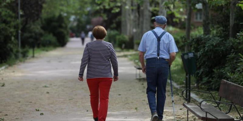 Una mujer y un hombre de edad avanzada con bastón caminando. EP