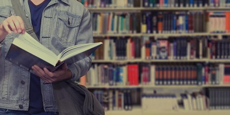 Un joven estudiante abre un libro en una biblioteca
