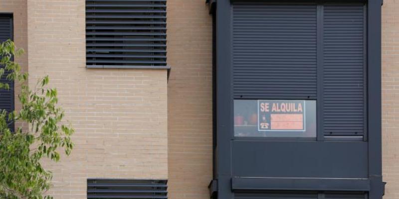 En la fachada de un edificio se ve un cartel de 'Se Alquila' bajo la persiana de uno de los pisos.