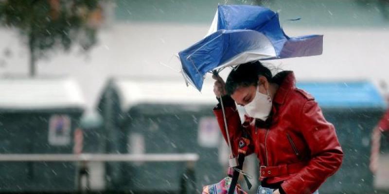 Un varón lucha contra el viento y la lluvia para que no le derribe el paraguas 