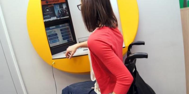 La eliminación de cajeros automáticos perjudica - Servimedia Una persona con discapacidad haciendo uso de cajeros automáticos