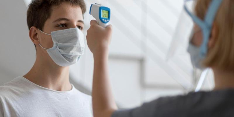 Una sanitaria toma la temperatura de un joven con mascarilla | Foto de Servimedia Una sanitaria toma la temperatura de un joven con mascarilla