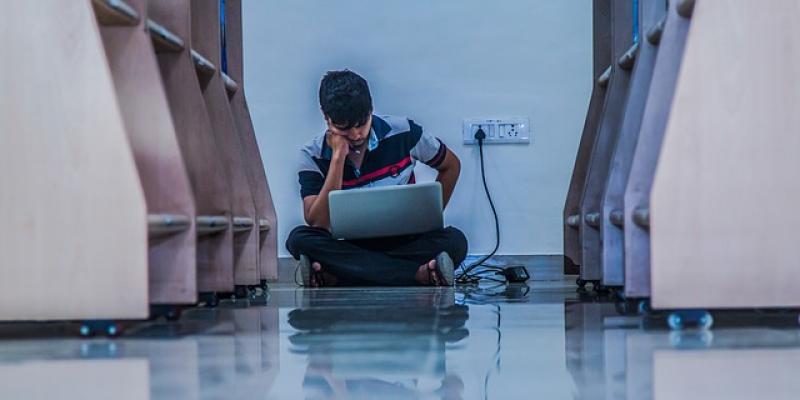 Estudiante de universidad con su ordenador sentado en el suelo de la biblioteca / Pixabay