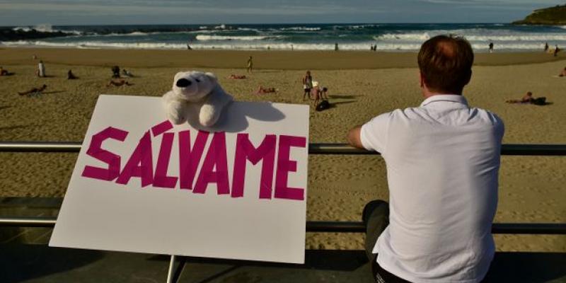 Un hombre descansa en la Playa de la Concha, de San Sebastián, junto a una pancarta en la que se lee "Sálvame". 