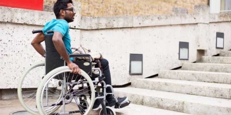 Hombre con discapacidad en silla de ruedas esperando en la parte inferior de una escalera