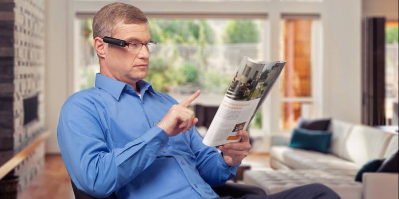 Señor con discapacidad visual utilizando OrCam MyEye para leer el periódico / OrCam Technologies