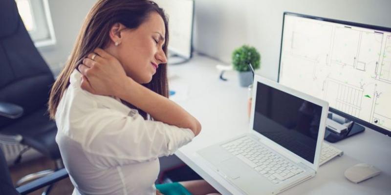 Mujer con dolores musculares trabajando con su ordenador / Objetivo bienestar
