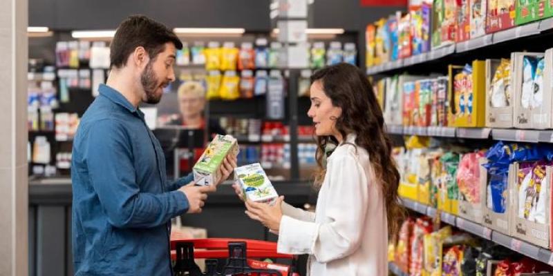 Ahorro en la compra | Foto de Dia Dos jóvenes, comparando precios en un supermercado
