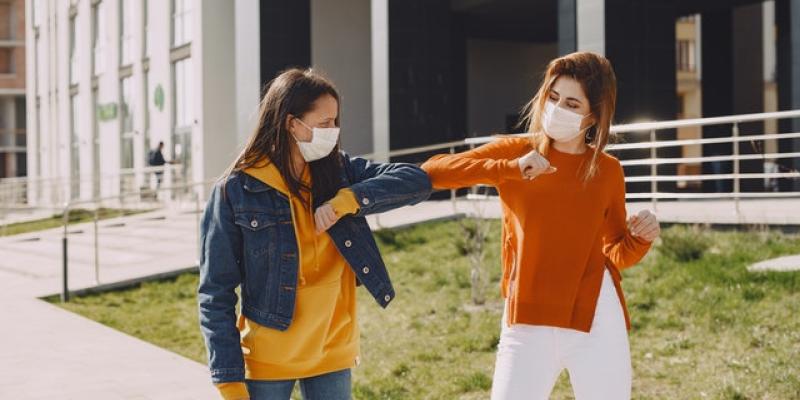 Imagen de dos chicas chocando el codo/CAF Recuperar la normalidad tras la pandemia