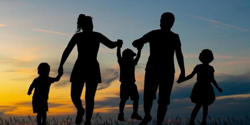 Imagen de una familia a contraluz. Se ven al padre y la madre, cogiendo de las manos a tres menores