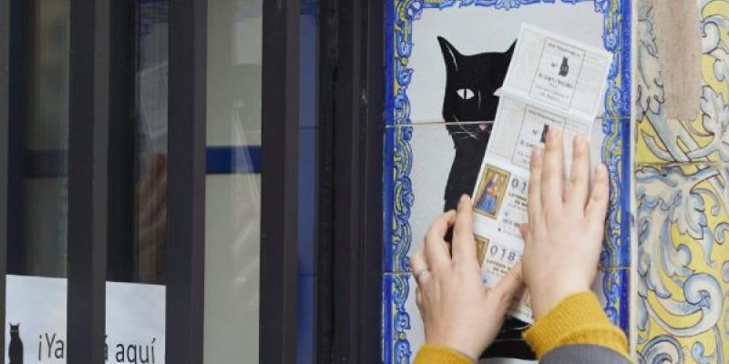 Una persona frota un billete de Lotería de Navidad por el azulejo de la Administración de Lotería el Gato Negro en Sevilla Joaquin Corchero / Europa Press Manos pasando décimos de lotería de Navidad por la imagen de un gato negro
