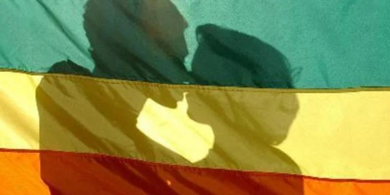 Pareja besándose tras una bandera LGTBI