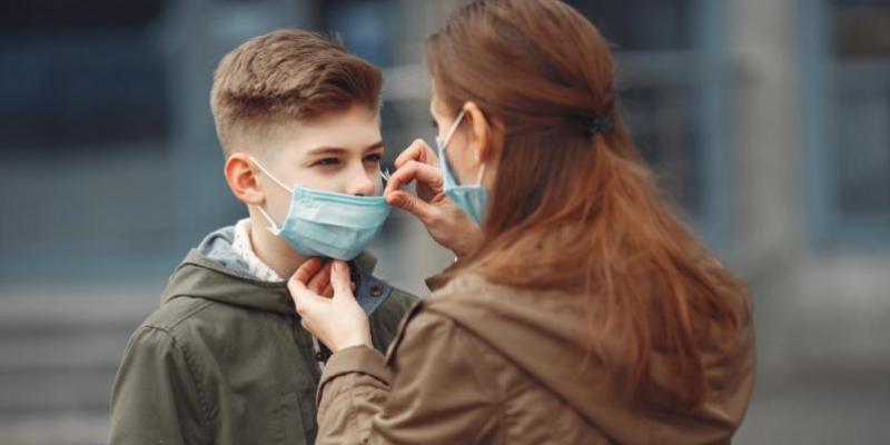 Una madre coloca la mascarilla de protección a su hijo 