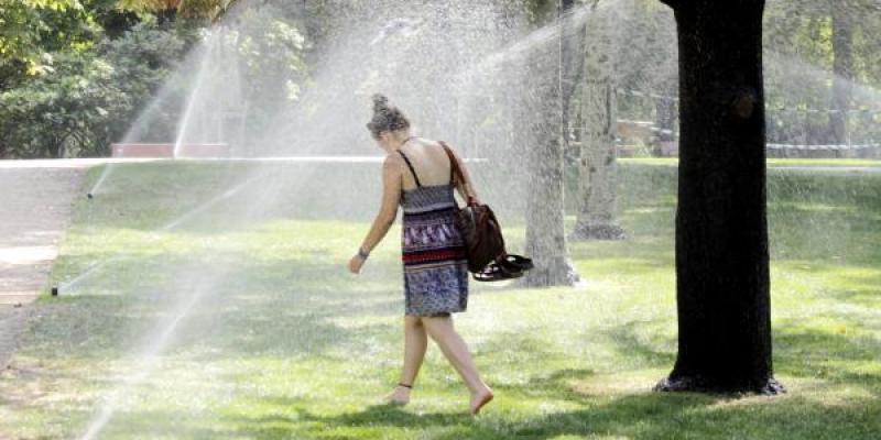Una joven se refresca con el riego de agua en un parque | Foto: Sofía González para Servimedia