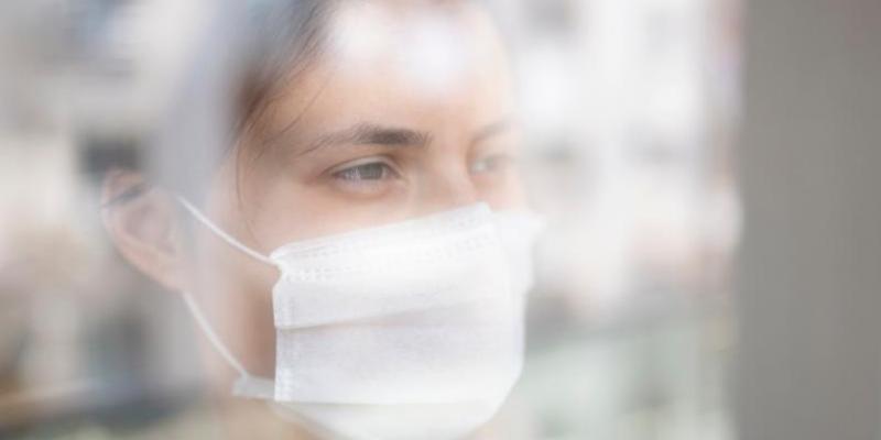 Tratamientos oncológicos Mujer con mascarilla mirando por la ventana / Foto: Farmaindustria