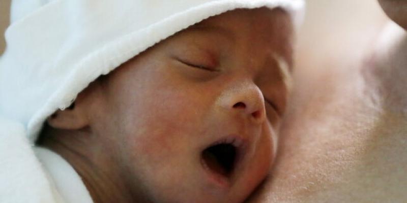 Un bebé con cará sonrosada y arropado con sábanas blancas deja ver su cara 