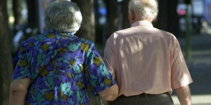 De espaldas, un matrimonio de personas mayores camina cogidos del brazo 