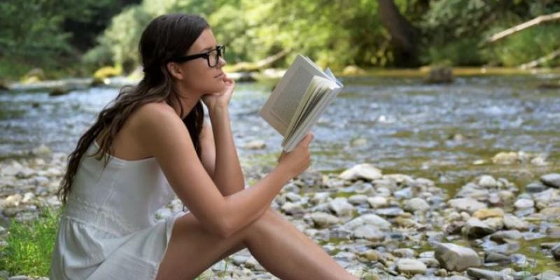 Chica leyendo un libro de poemas en la orilla de un río