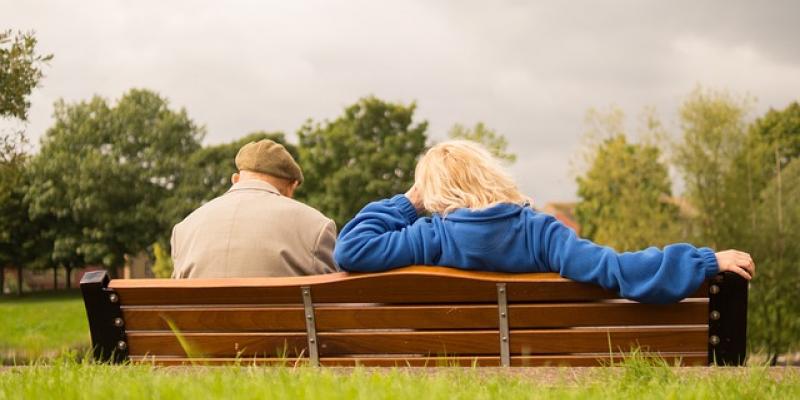 Un señor mayor y una mujer adulta sentados en un banco de espaldas