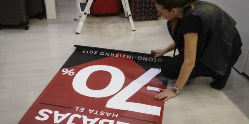 Imagen de una mujer poniendo el cartel de las rebajas/El Mundo Las rebajas de este 2022 vienen con trampas