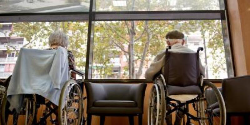 Dos ancianos en silla de ruedas disfrutan de las vistas a través de una ventana