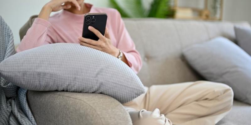 Una mujer sentada en el sofá, con el móvil 