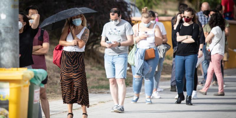 Una mujer se protege del sol con un paraguas en la cola de la vacunación