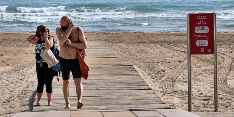 Dos bañistas salen de una playa con sus mascarillas.