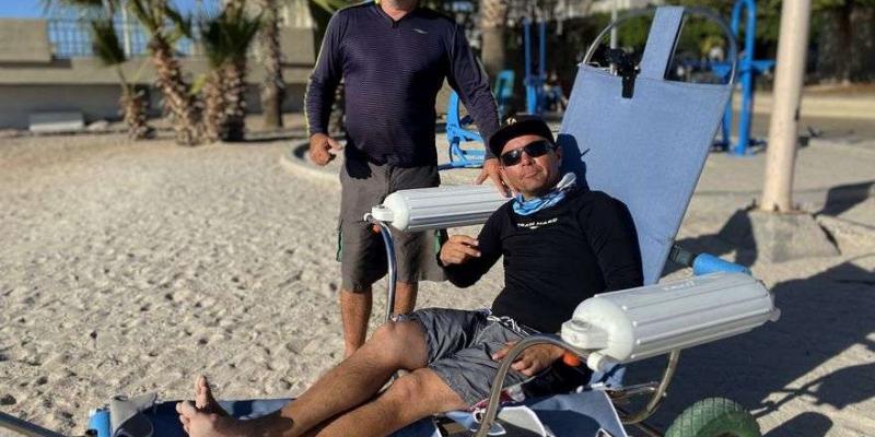Un joven con movilidad reducida, prueba la silla anfibia en la playa