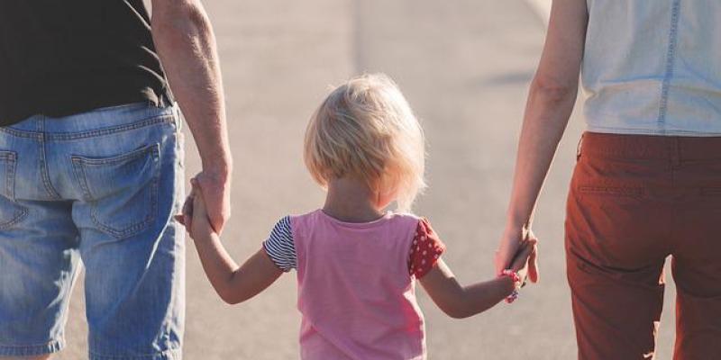 Un padre y una madre cogen de la mano a su hija