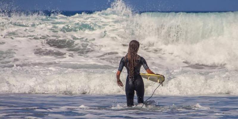 Una surfista se va metiendo en el mar con su tabla