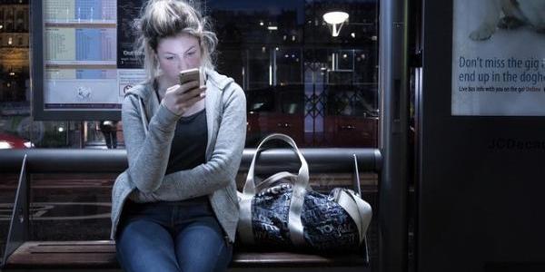 Chica mirando el móvil en una parada de autobús