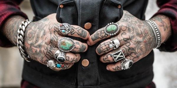 Hombre sujetando el centro de su camisa con sus manos totalmente tatuadas / Pixabay
