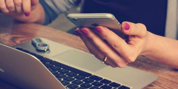 Mujer sosteniendo su Iphone con su Macbook en el escritorio