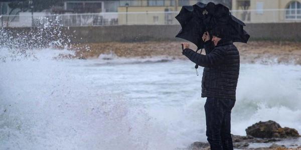 Un hombre observando la mar, mientras que intenta sujetar el paraguas y no mojarse. Foto de Sergio G. Cañizares, EFE