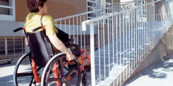 Una mujer en silla de ruedas accede al portal de un edificio de viviendas.