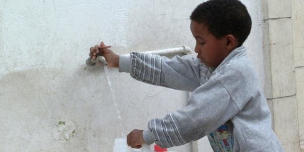 Un niño usando el suministro de agua en Libia